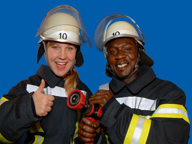 Eine Feuerwehrfrau und ein Feuerwehrmann mit unterschiedlichen Hautfarben signalisieren mit dem typischen Daumen hoch, dass die Feuerwehren international sind.