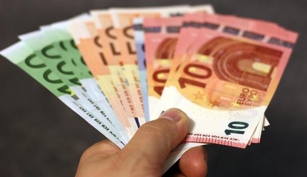 Eine Hand hlt mehrere aufgefcherte Euro-Geldschein zur bergabe bereit.