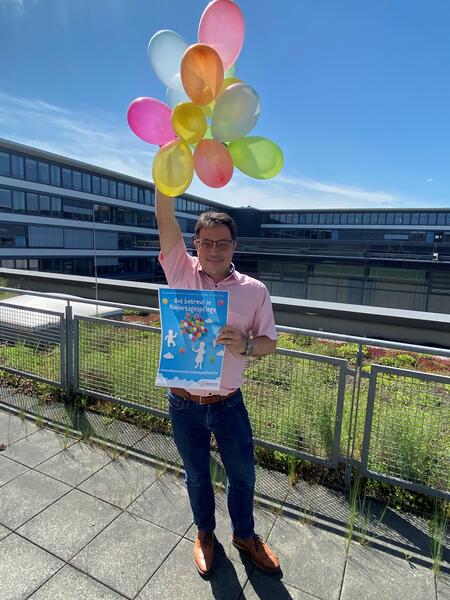 Kreisbeigeordneter Carsten Müller wirbt mit Plakat und Luftballons für die Bundesweite Aktionswoche 2022 "Gut betreut in Kindertagespflege".