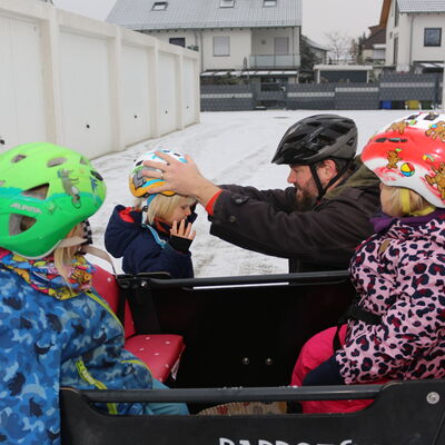 Tagesvater zieht den Kindern Helme auf, um mit dem Lastenrad zu starten