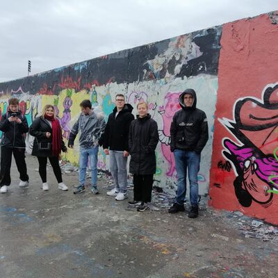 Teilnehmende des Bildungsurlaubs stehen vor einem bemalten Stück der Berliner Mauer.