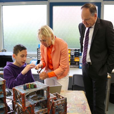 Ein Schüler zeigt Digitalministerin Prof. Dr. Kristina Sinemus und Landrat Oliver Quilling, wie er mit Airbrush das Gebäude aus dem 3D-Drucker bemalt hat.